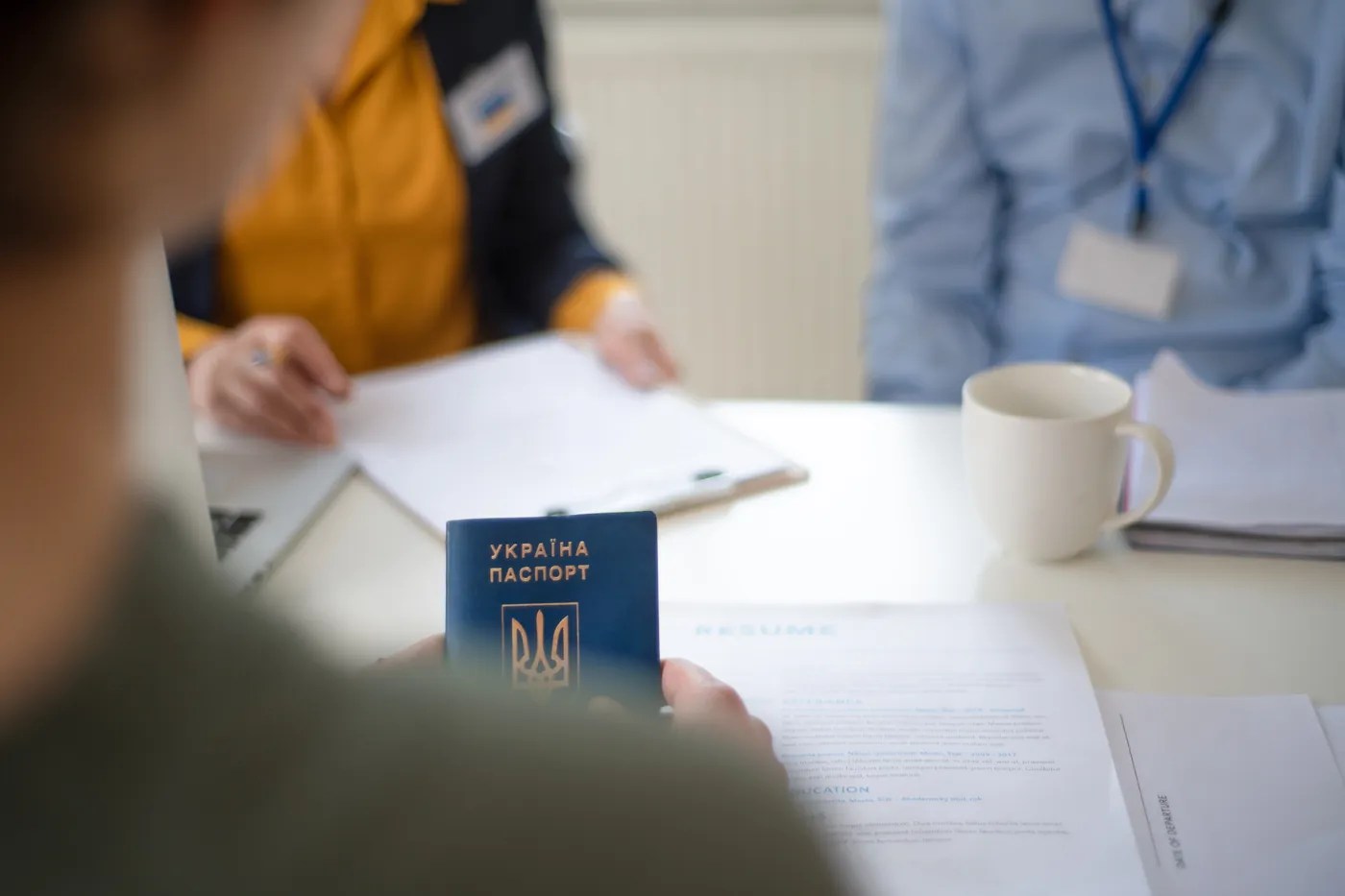 Iemand houdt een Oekraïens paspoort vast aan een balie met formulieren, terwijl een medewerker de papieren doorneemt